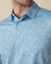 Men's Ka'anapali Polo in Coastal, collar detail view featuring an allover white tropical floral and palm leaf line-art print on a medium blue performance fabric