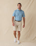 Men's Ka'anapali Polo in Coastal, full length model view featuring a medium blue short sleeve polo with an allover white tropical floral and palm leaf line-art print, styled with khaki shorts and white shoes