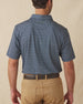 Men's Redbud Polo in New Indigo, back view on model featuring a navy base with a scattered green and light pink floral print and green Straight Down logo embroidered at upper back, paired with khaki pants