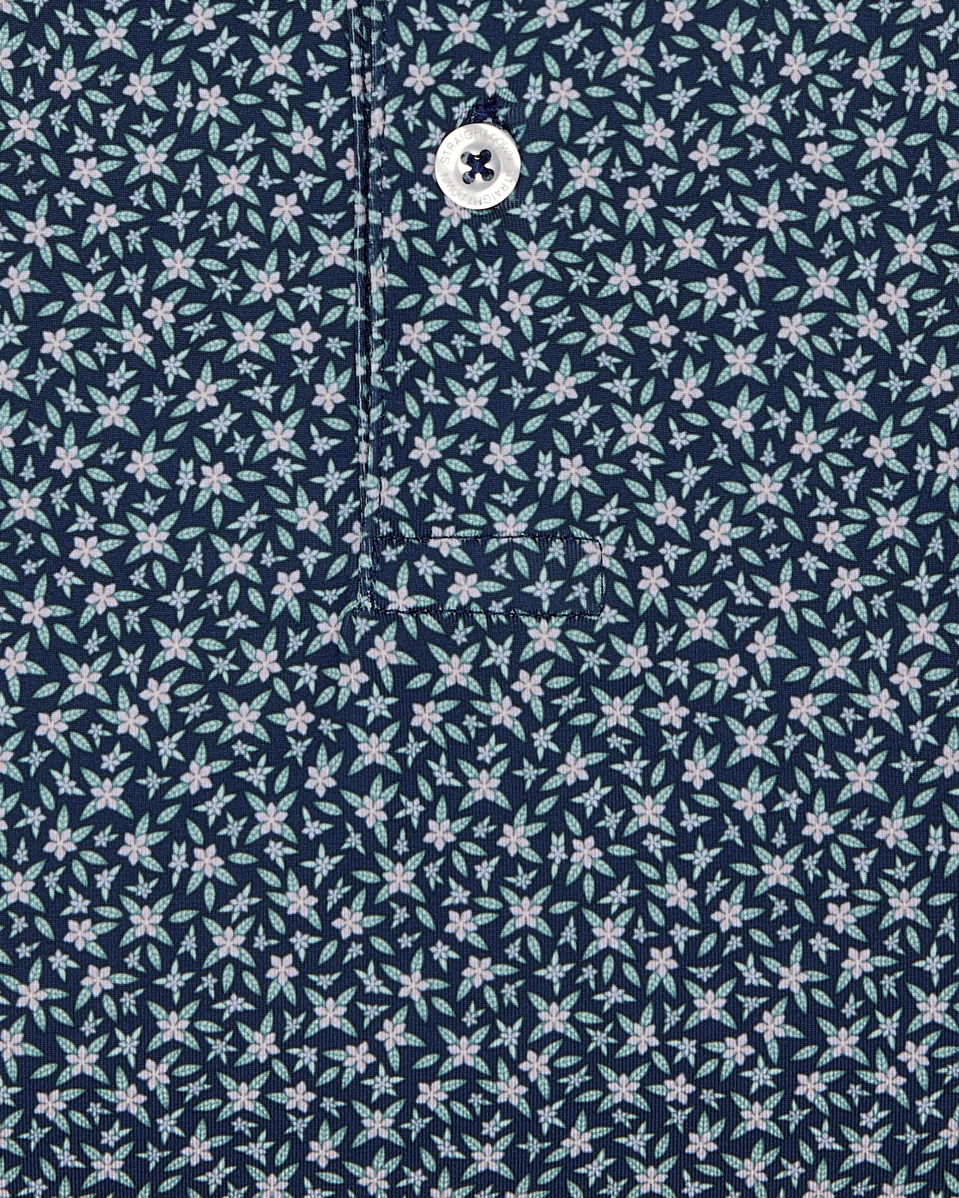 Men's Redbud Polo in New Indigo, close-up detail view featuring navy base with scattered green and light pink floral print and Straight Down logo engraved button with placket detail