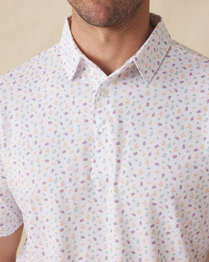 Men's Pimento Cheese Polo in White, close-up front view on model highlighting a scattered golf, sandwich, and drink print in purple, teal, and orange on a white base
