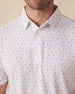 Men's Pimento Cheese Polo in White, close-up front view on model highlighting a scattered golf, sandwich, and drink print in purple, teal, and orange on a white base