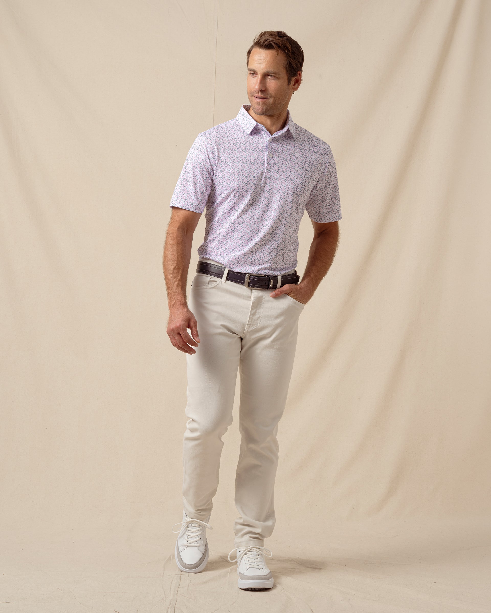 Men’s light pink polo with chili pepper print paired with off-white pants, brown belt, and white sneakers