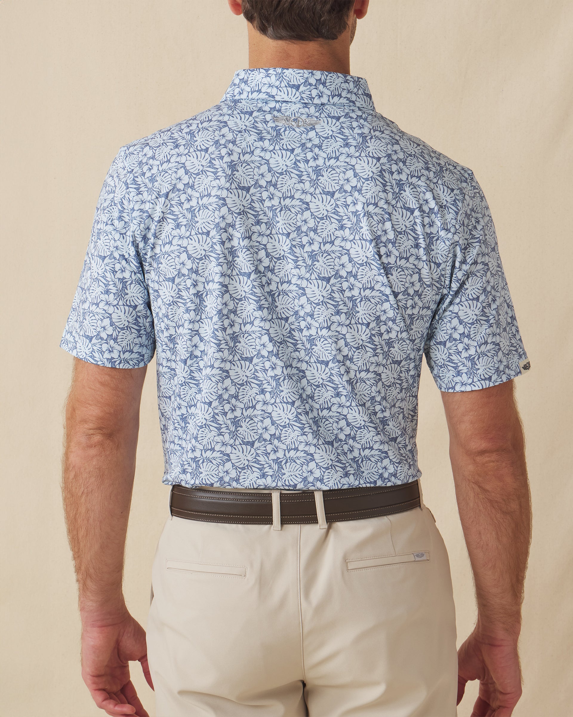 Men's Lihu'e Polo in Sea Spray, back model view featuring a light blue short sleeve polo with an allover navy hibiscus flower and monstera leaf print, with an embroidered Straight Down logo at the back collar