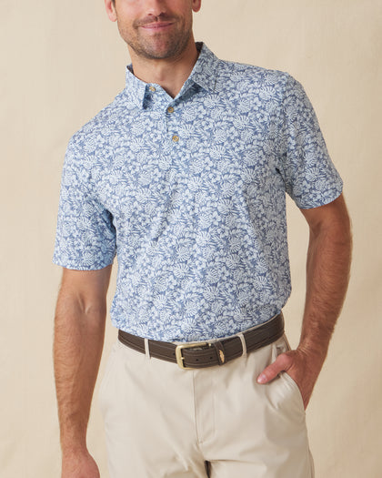 Men's Lihu'e Polo in Sea Spray, front model view featuring a light blue short sleeve polo with an allover navy hibiscus flower and monstera leaf print, styled with khaki pants and a leather belt