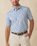 Men's Lihu'e Polo in Sea Spray, front model view featuring a light blue short sleeve polo with an allover navy hibiscus flower and monstera leaf print, styled with khaki pants and a leather belt