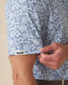 Men's Lihu'e Polo in Sea Spray, sleeve detail view featuring a light blue short sleeve polo with an allover navy hibiscus flower and monstera leaf print, with a Straight Down logo tab on the sleeve hem