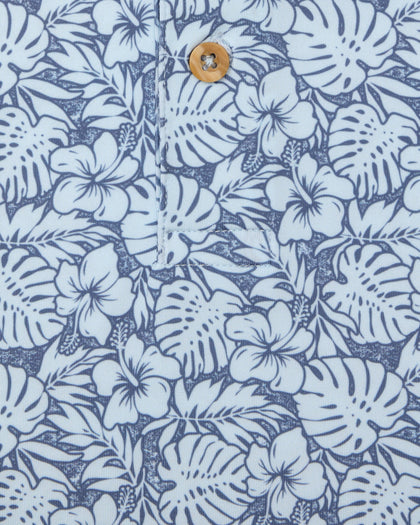 Men's Lihu'e Polo in Sea Spray, close-up fabric detail view featuring an allover navy hibiscus flower and monstera leaf print on a light blue performance fabric with a natural wood-tone button