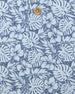 Men's Lihu'e Polo in Sea Spray, close-up fabric detail view featuring an allover navy hibiscus flower and monstera leaf print on a light blue performance fabric with a natural wood-tone button