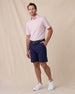 Full-length view of a male model wearing the Channel Stripe Polo in Seashell with navy shorts, a navy belt, and white shoes.