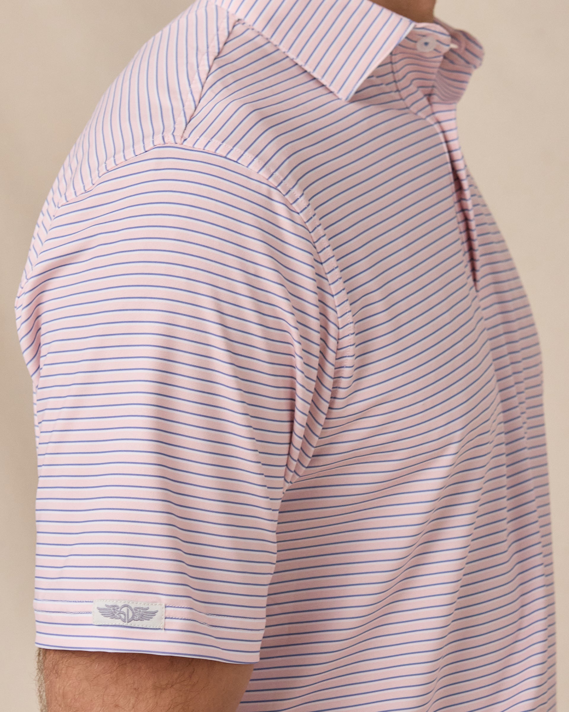 Close-up side view of the Channel Stripe Polo in Seashell, highlighting the shoulder construction, striped fabric, and logo detail on the sleeve.
