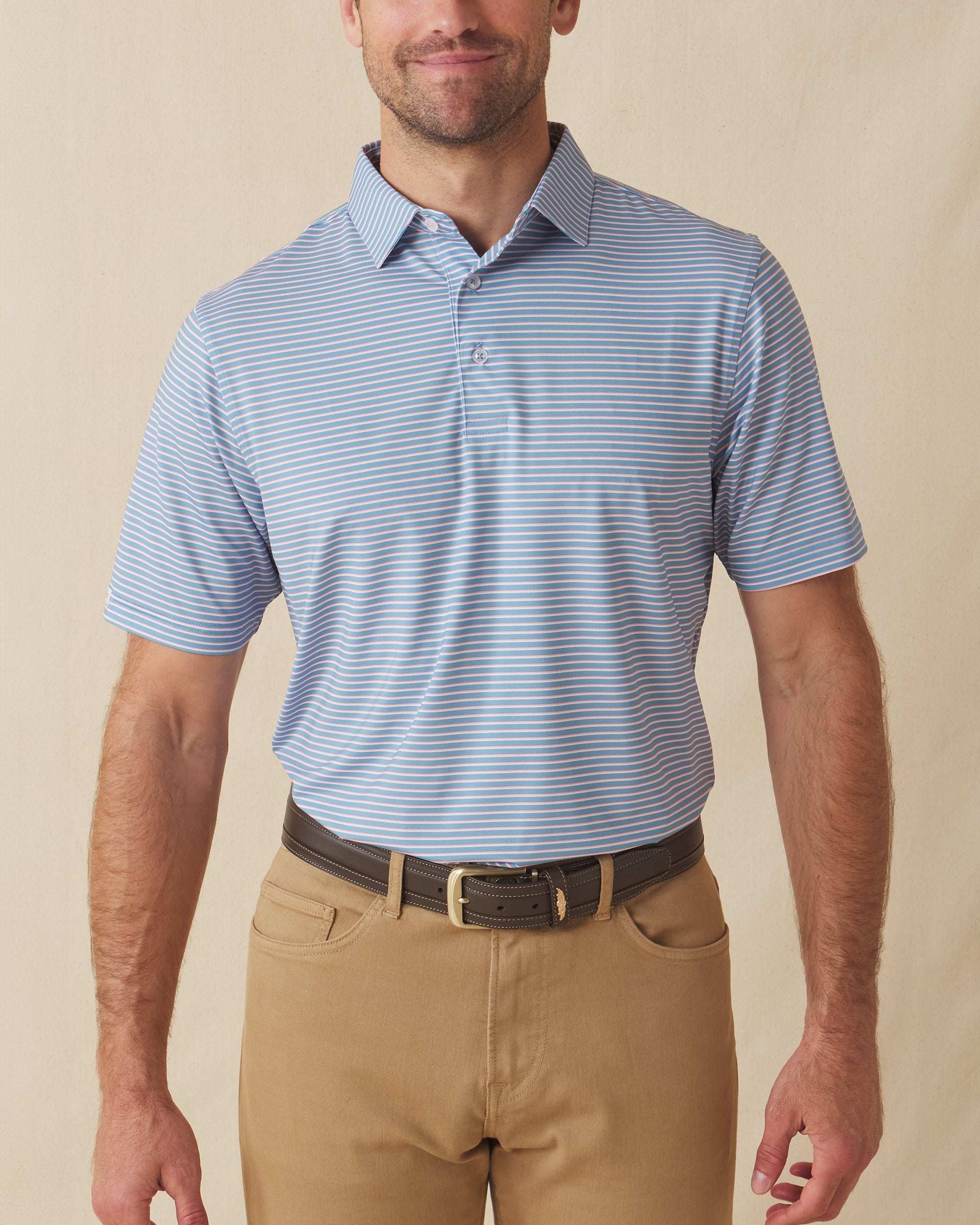 Men's Channel Stripe Polo in Coastal, front model view featuring a light blue short sleeve polo with horizontal pink and white stripes, styled with tan pants and a leather belt