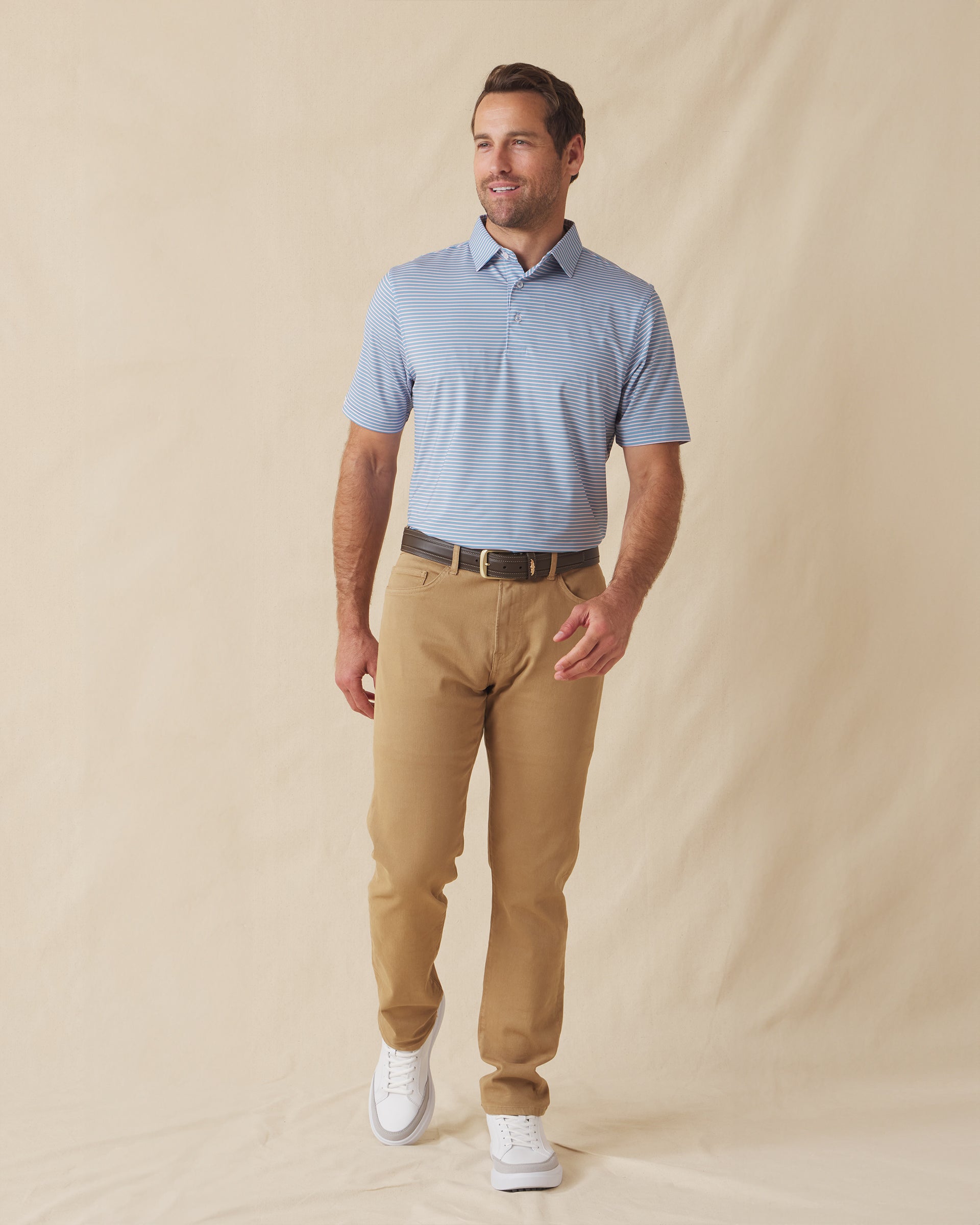 Men's Channel Stripe Polo in Coastal, full length model view featuring a light blue short sleeve polo with horizontal pink and white stripes, styled with tan pants and white shoes