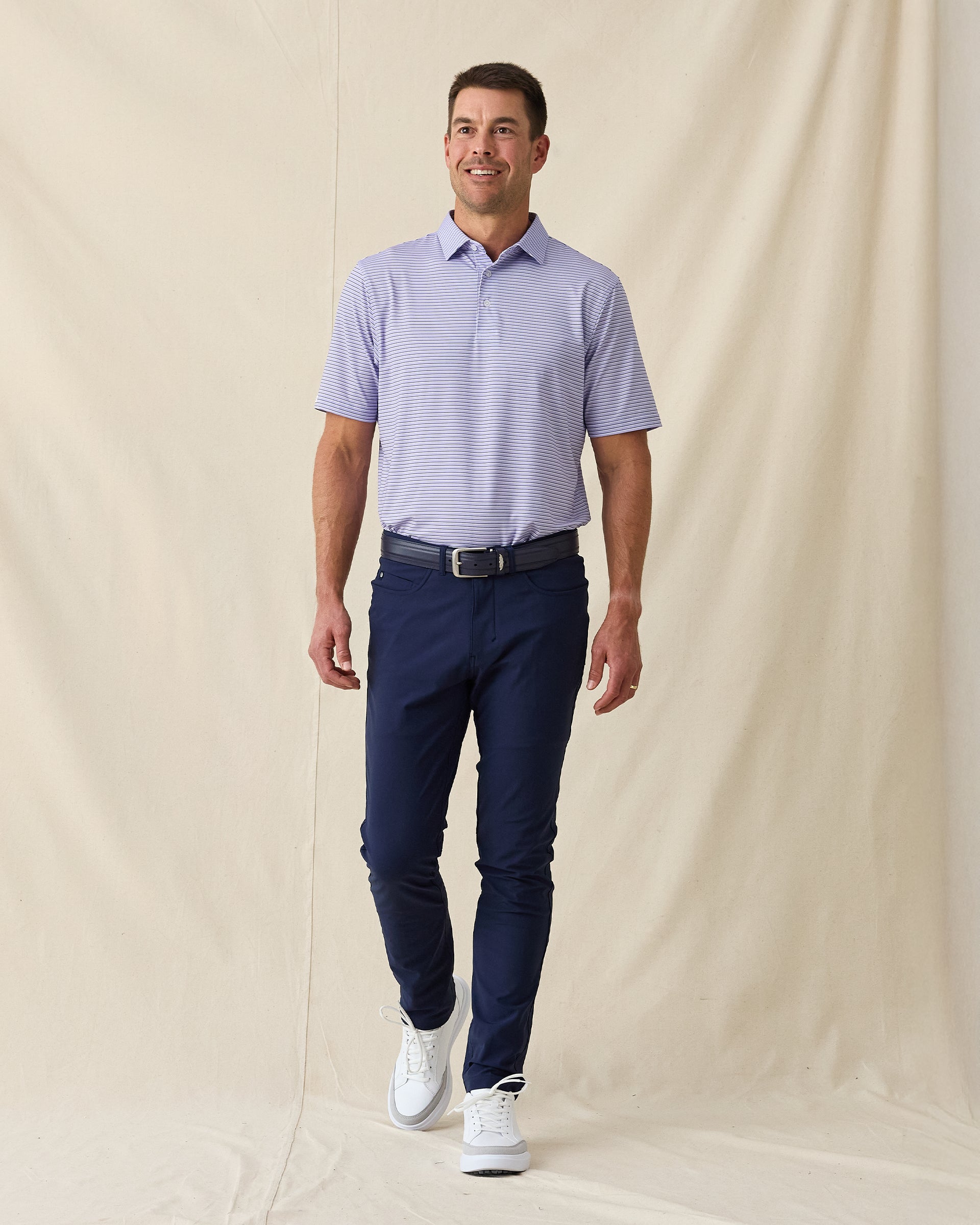 Men's Channel Stripe Polo in Violet, full length model view featuring a lavender short sleeve polo with horizontal navy and white pencil stripes paired with navy pants and white shoes