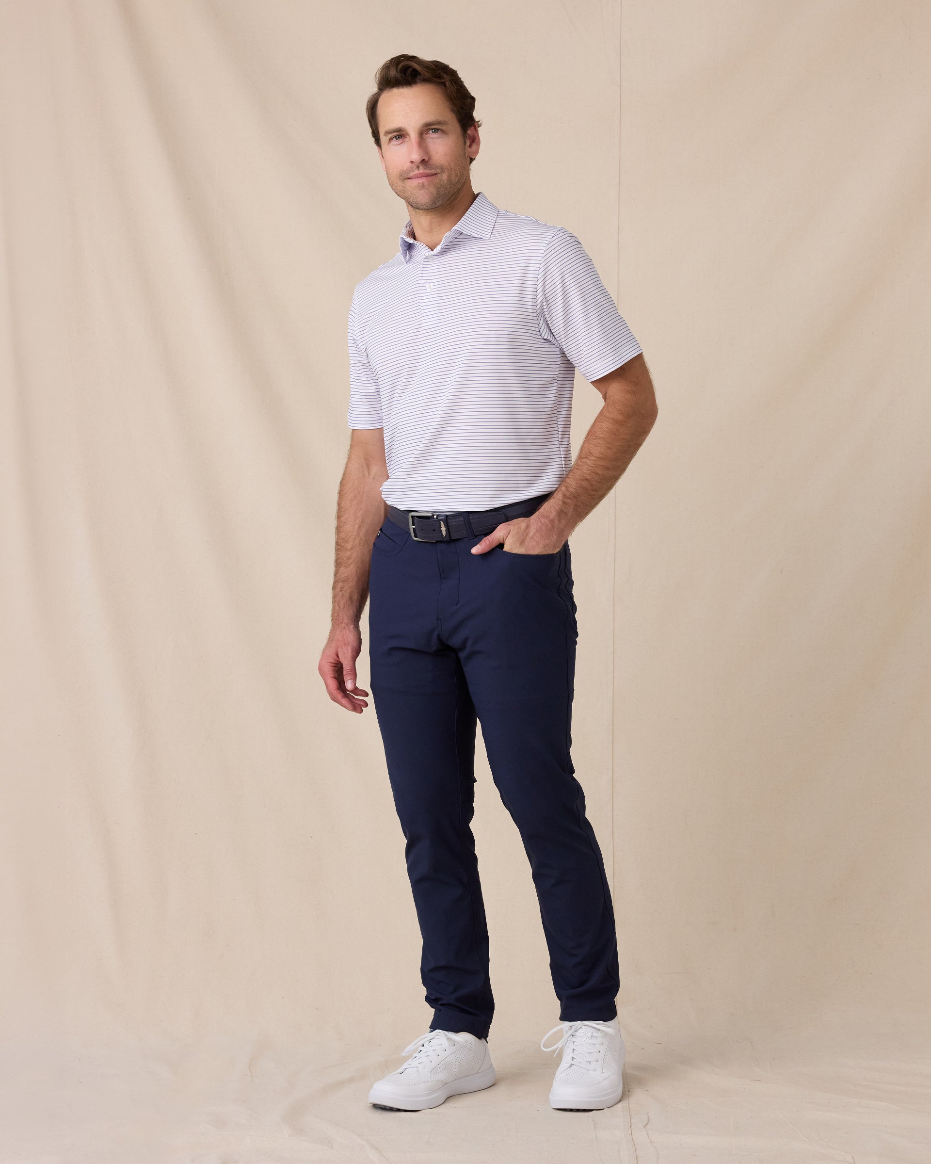 Model wearing the Men's Channel Stripe Golf Polo in White with navy golf pants and white golf shoes.