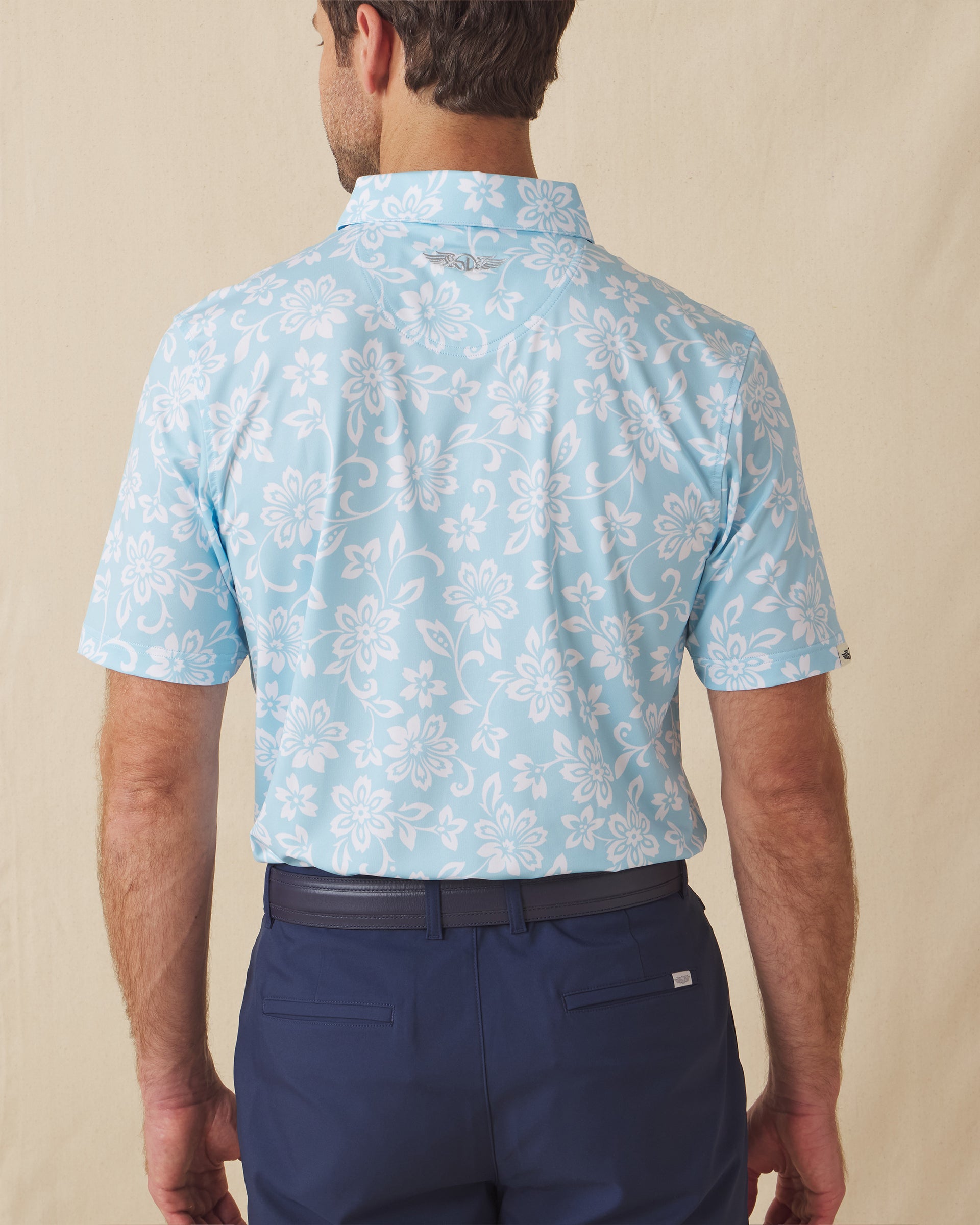 Men's Napali Coast Polo in Gemstone, back model view featuring a light aqua blue short sleeve polo with an allover white Hawaiian floral and vine print, with an embroidered Straight Down logo at the back collar
