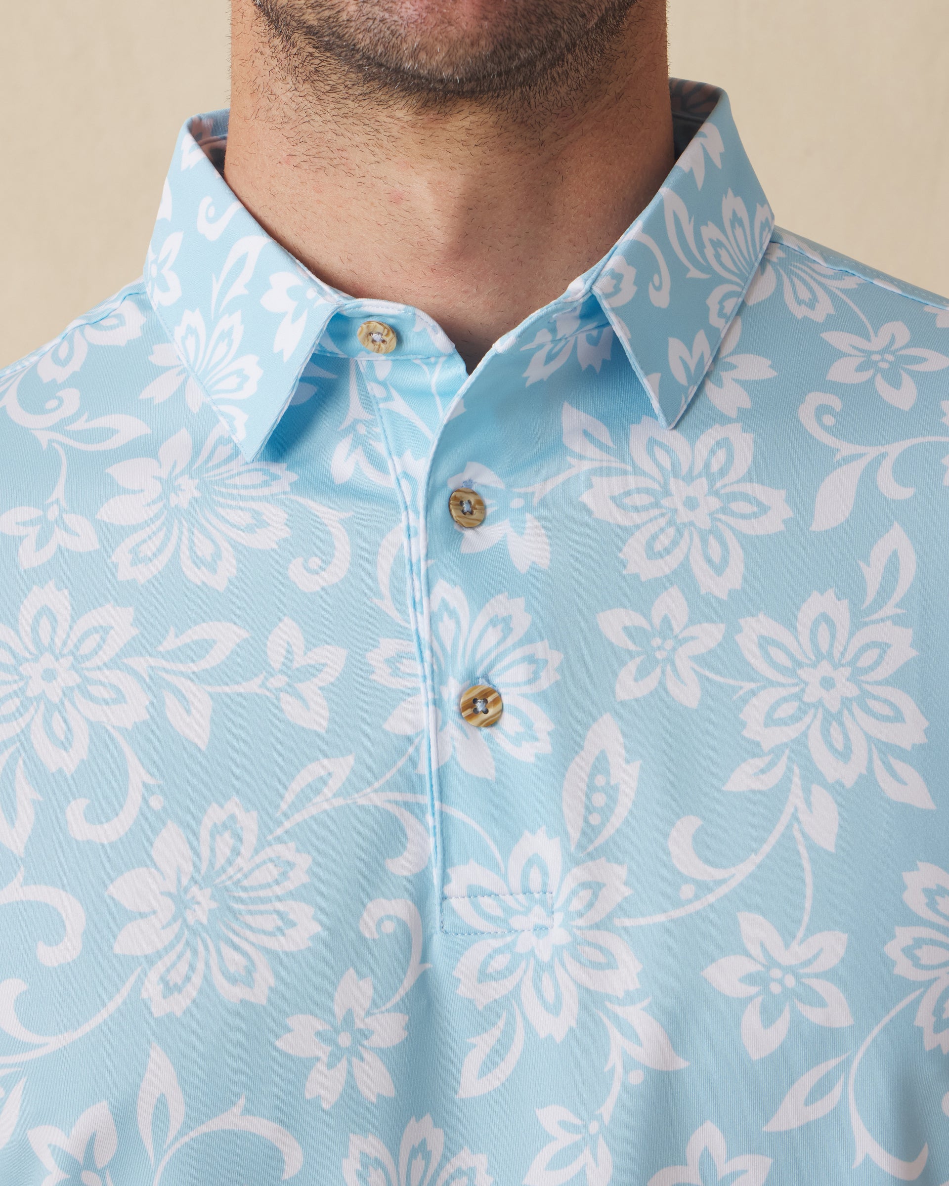 Men's Napali Coast Polo in Gemstone, collar detail view featuring an allover white Hawaiian floral and vine print on a light aqua blue performance fabric with natural wood-tone buttons