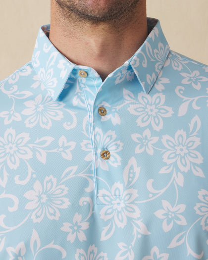Men's Napali Coast Polo in Gemstone, collar detail view featuring an allover white Hawaiian floral and vine print on a light aqua blue performance fabric with natural wood-tone buttons