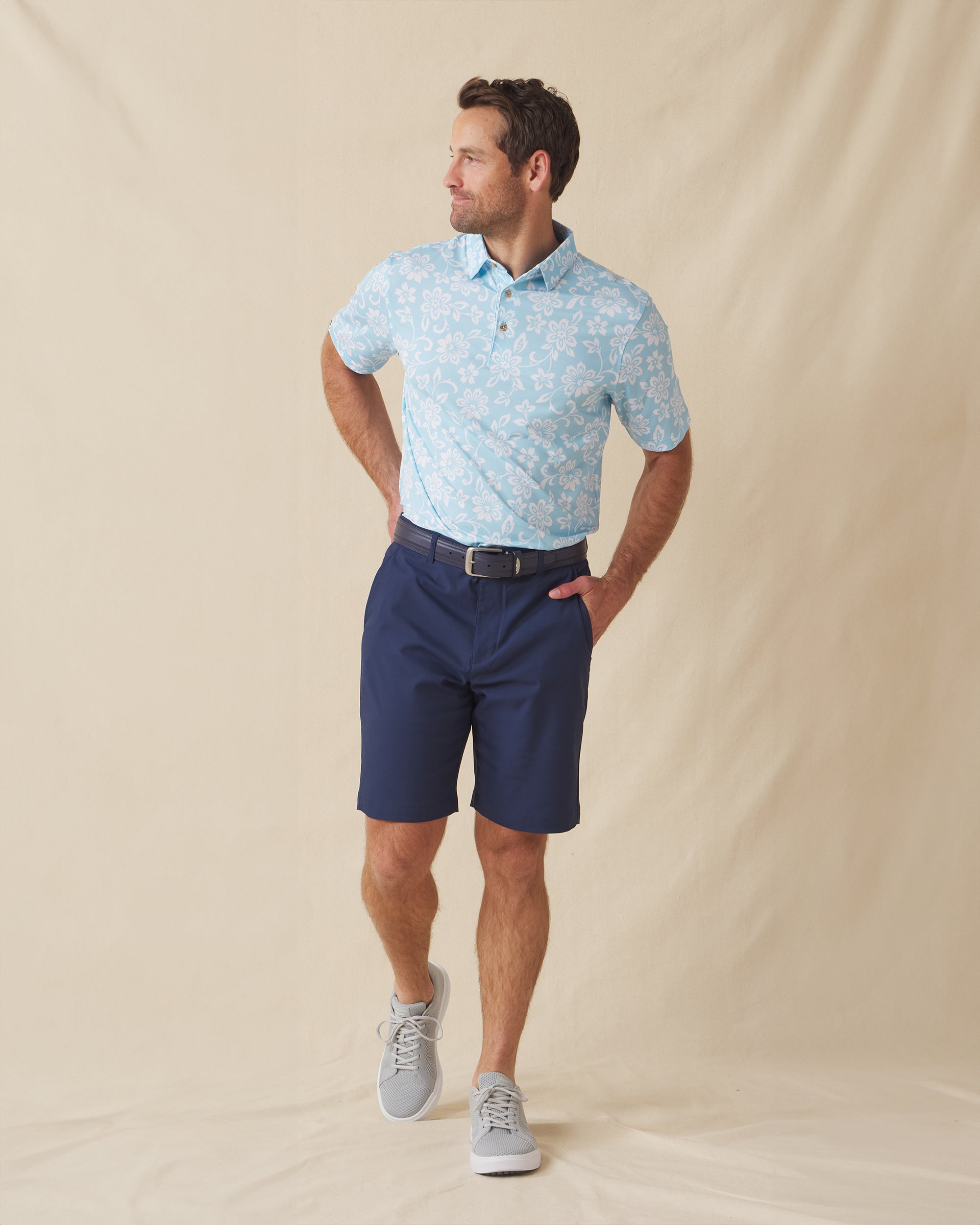 Men's Napali Coast Polo in Gemstone, full length model view featuring a light aqua blue short sleeve polo with an allover white Hawaiian floral and vine print, styled with navy shorts and gray shoes