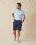 Men's Napali Coast Polo in Gemstone, full length model view featuring a light aqua blue short sleeve polo with an allover white Hawaiian floral and vine print, styled with navy shorts and gray shoes
