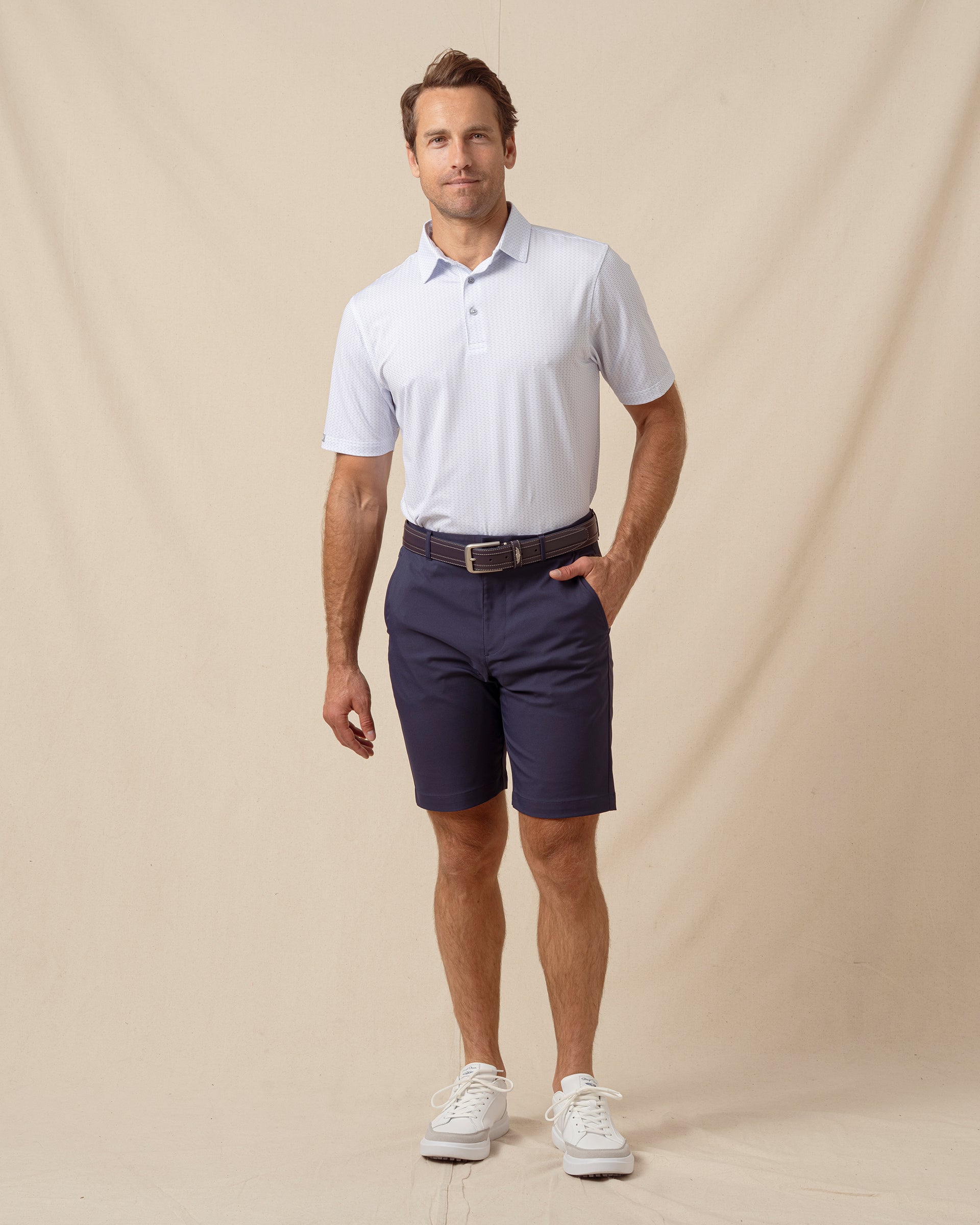 Men’s light blue shark print performance polo styled with navy shorts, belt, and white sneakers