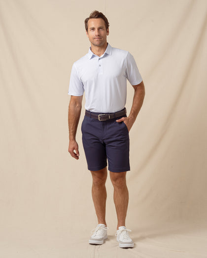 Men’s light blue shark print performance polo styled with navy shorts, belt, and white sneakers