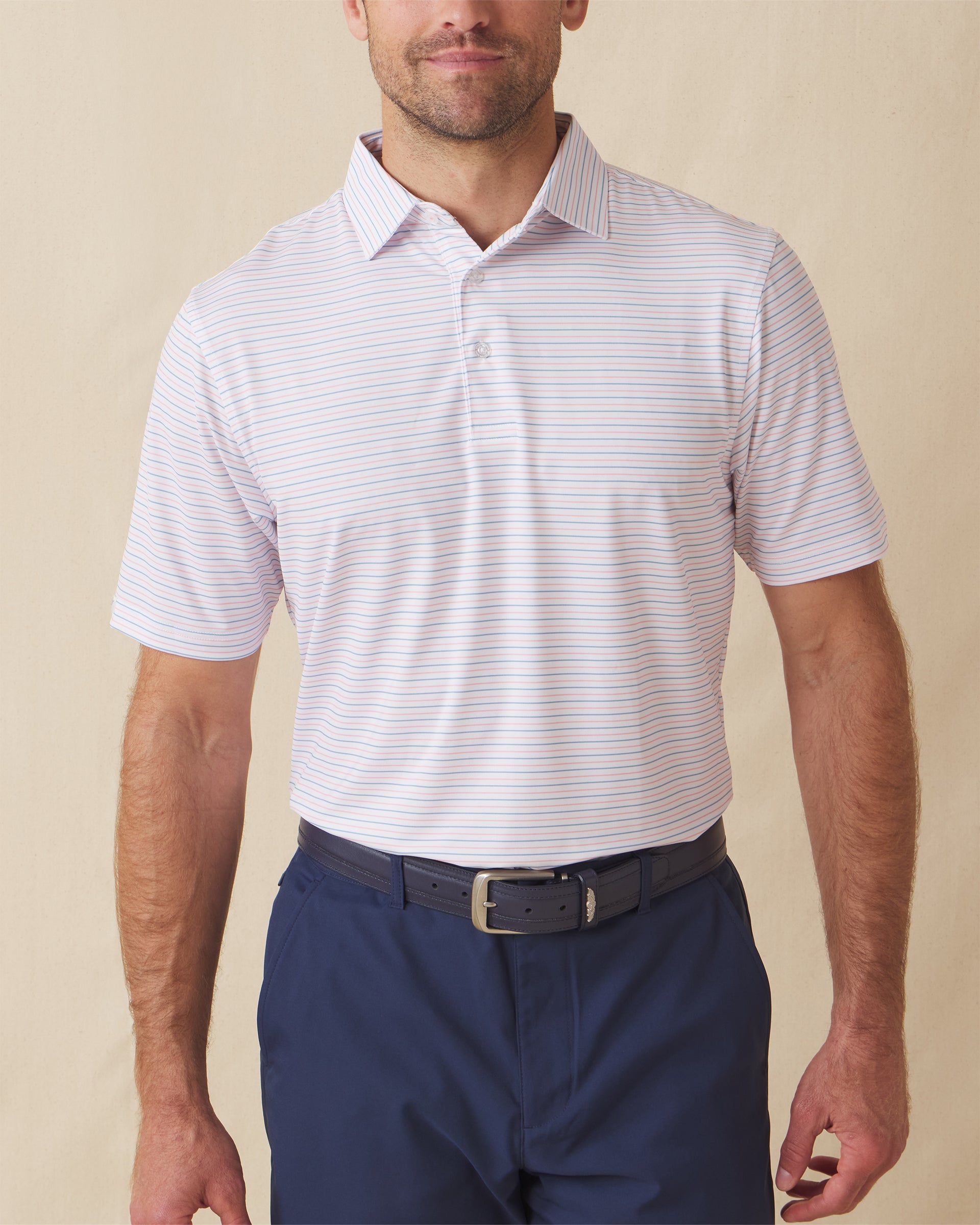Men's Preserve Stripe Polo in Spritz, front model view featuring a white short sleeve polo with horizontal pink and blue pinstripes, styled with navy pants and a leather belt