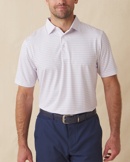 Men's Preserve Stripe Polo in Spritz, front model view featuring a white short sleeve polo with horizontal pink and blue pinstripes, styled with navy pants and a leather belt