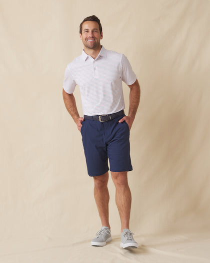Men's Preserve Stripe Polo in Spritz, full length model view featuring a white short sleeve polo with horizontal pink and blue pinstripes, styled with navy shorts and gray shoes
