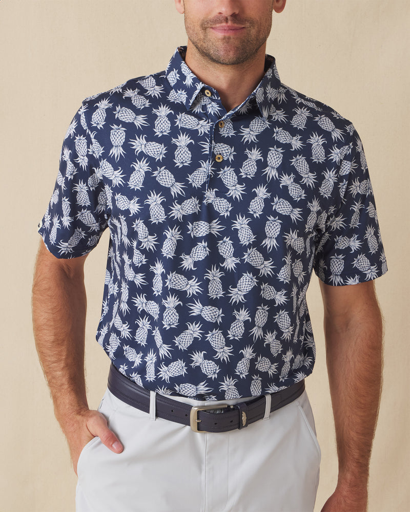 Men's Pineapple Express Polo in New Indigo, front view on model featuring a navy and white pineapple print with wood buttons, styled with light grey pants and a navy belt