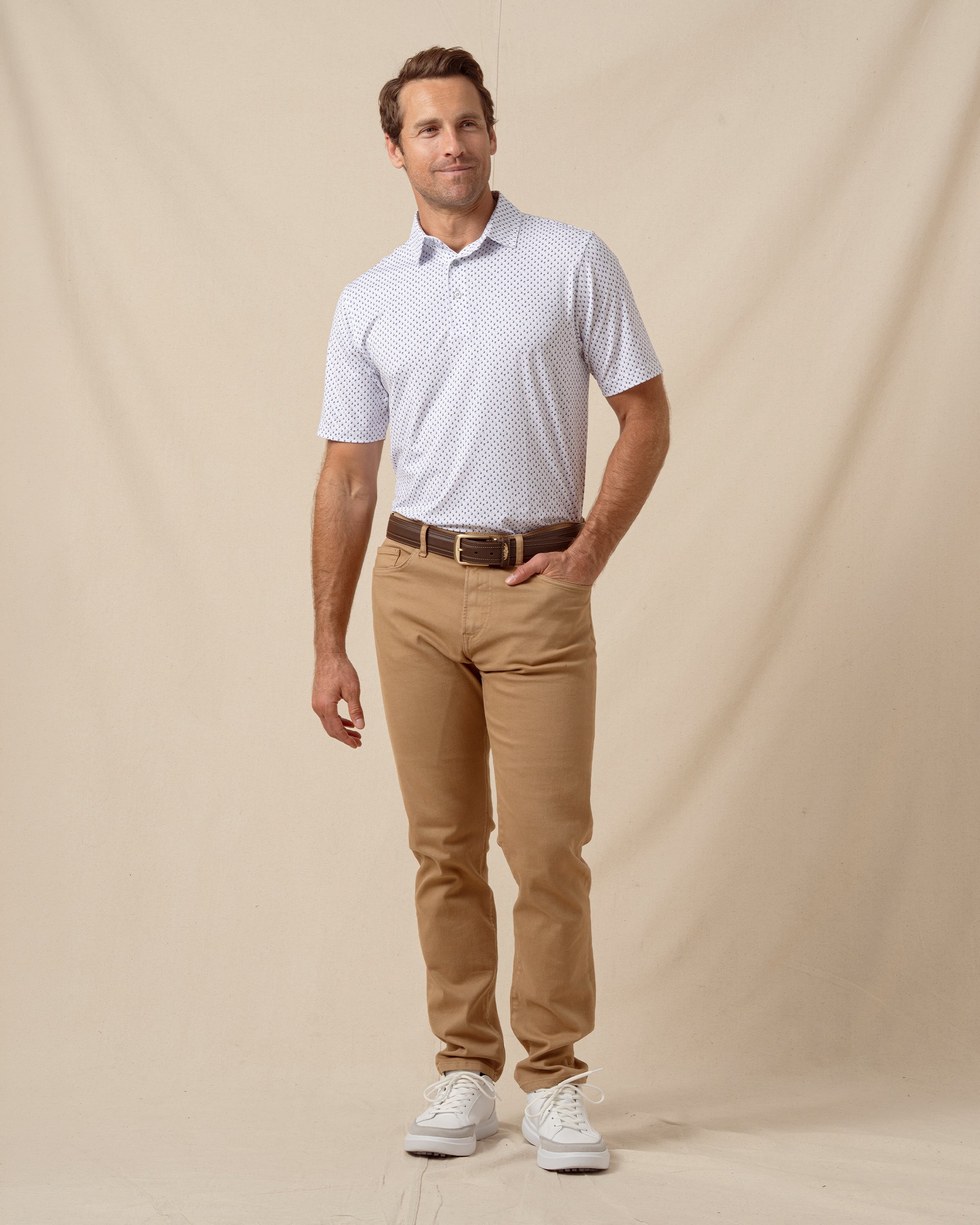 Men’s white geometric print polo shirt styled with tan pants, brown belt, and white sneakers