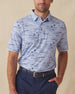 Men's Outrigger Polo in Powder, front view on model featuring a light blue Hawaiian scenic print with wood buttons, styled with navy pants and a navy belt