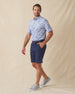 Men's Outrigger Polo in Powder, full-length side view on model featuring a light blue Hawaiian scenic print, styled with navy shorts and grey shoes