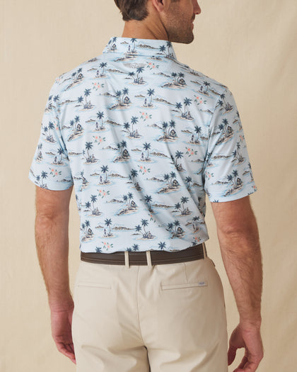 Men's Land Of Aloha Polo in Sea Spray, back model view featuring a light blue short sleeve polo with an allover Hawaiian island scene print with palm trees, thatched huts, hula dancers, outrigger canoes, and hibiscus flowers, with an embroidered Straight Down logo at the back collar
