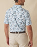 Men's Land Of Aloha Polo in Sea Spray, back model view featuring a light blue short sleeve polo with an allover Hawaiian island scene print with palm trees, thatched huts, hula dancers, outrigger canoes, and hibiscus flowers, with an embroidered Straight Down logo at the back collar