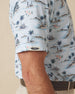 Men's Land Of Aloha Polo in Sea Spray, sleeve detail view featuring a light blue short sleeve polo with an allover Hawaiian island scene print, with a Straight Down logo tab on the sleeve hem