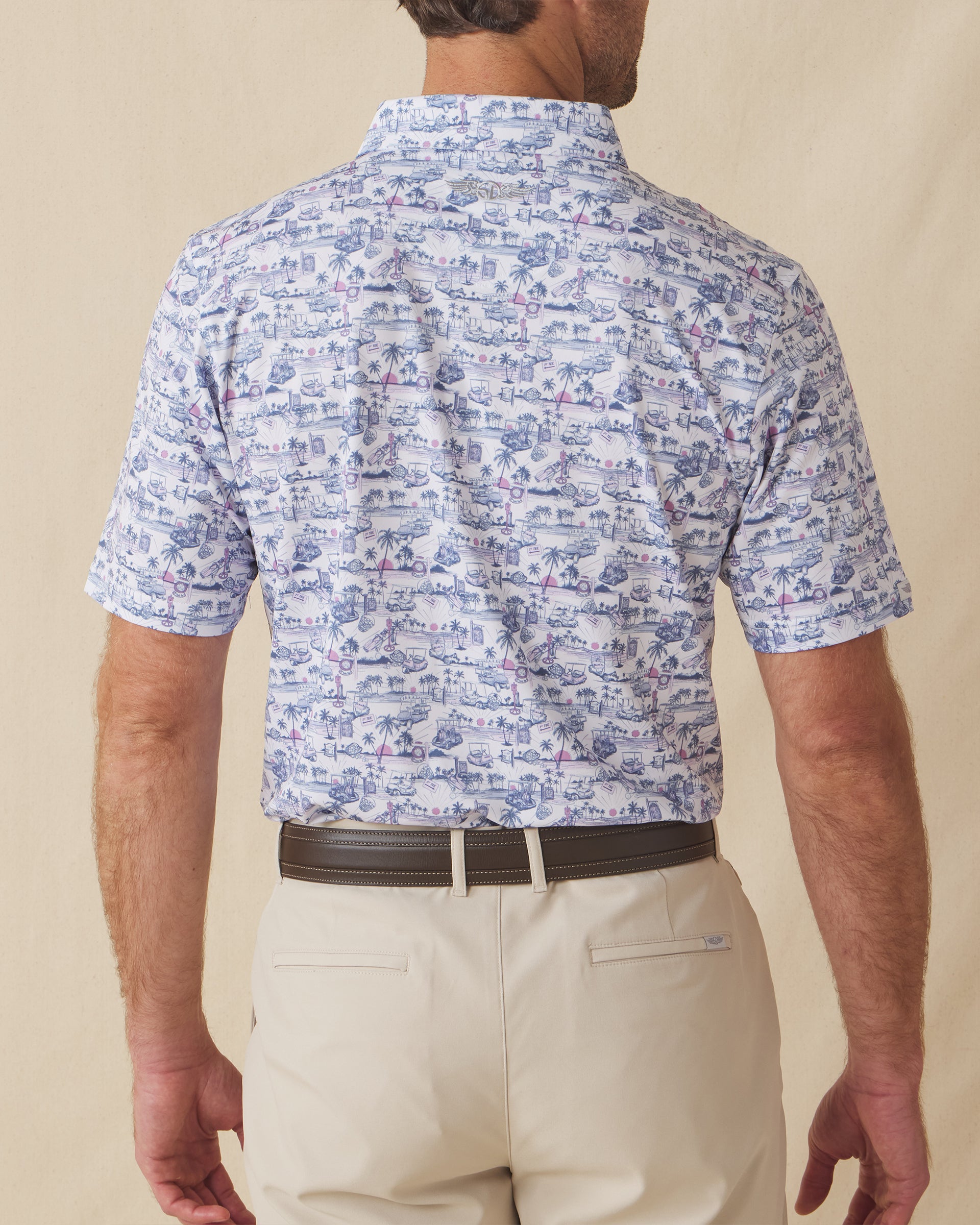 Back view of men’s white polo with blue and pink tropical golf print worn with beige shorts