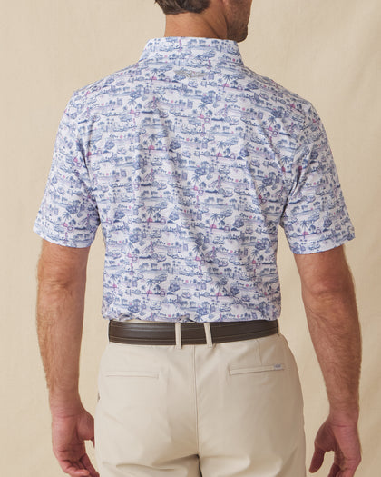 Back view of men’s white polo with blue and pink tropical golf print worn with beige shorts