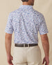 Back view of men’s white polo with blue and pink tropical golf print worn with beige shorts