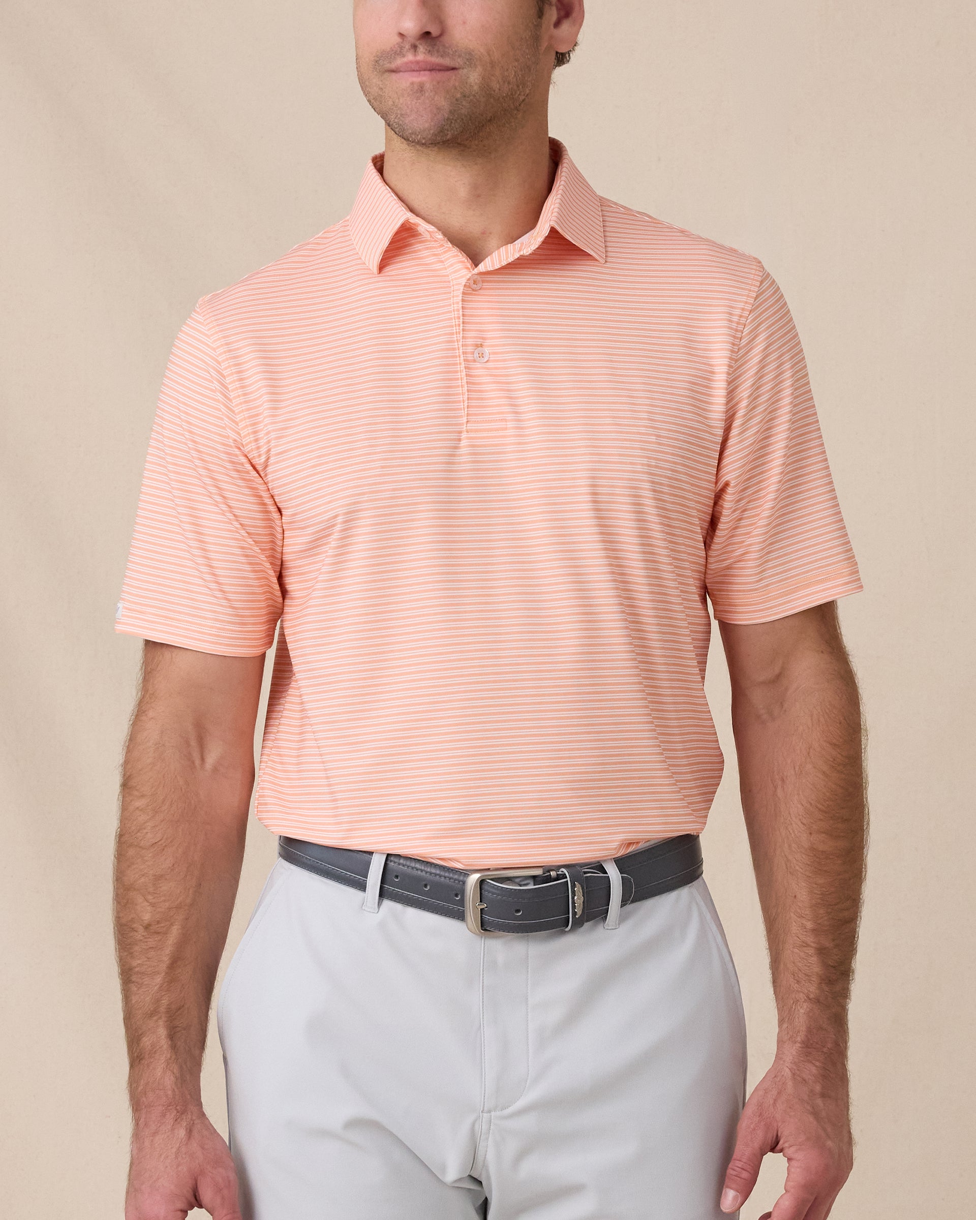 Model wearing the Campus Stripe Polo in Cantaloupe with white horizontal stripes, paired with light gray golf pants.