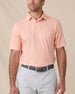 Model wearing the Campus Stripe Polo in Cantaloupe with white horizontal stripes, paired with light gray golf pants.