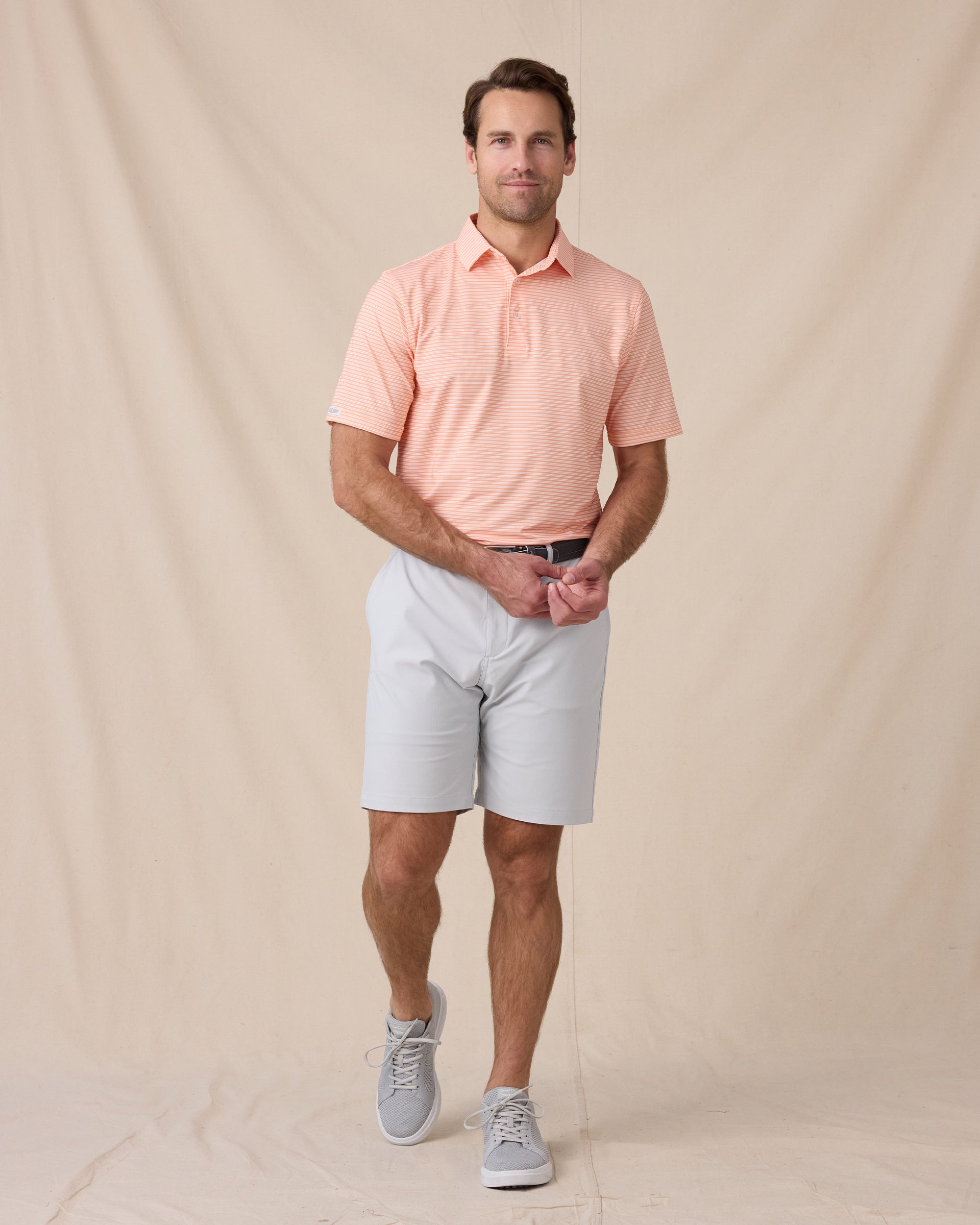 Model wearing the Campus Stripe Polo in Cantaloupe with light gray golf shorts and gray sneakers.
