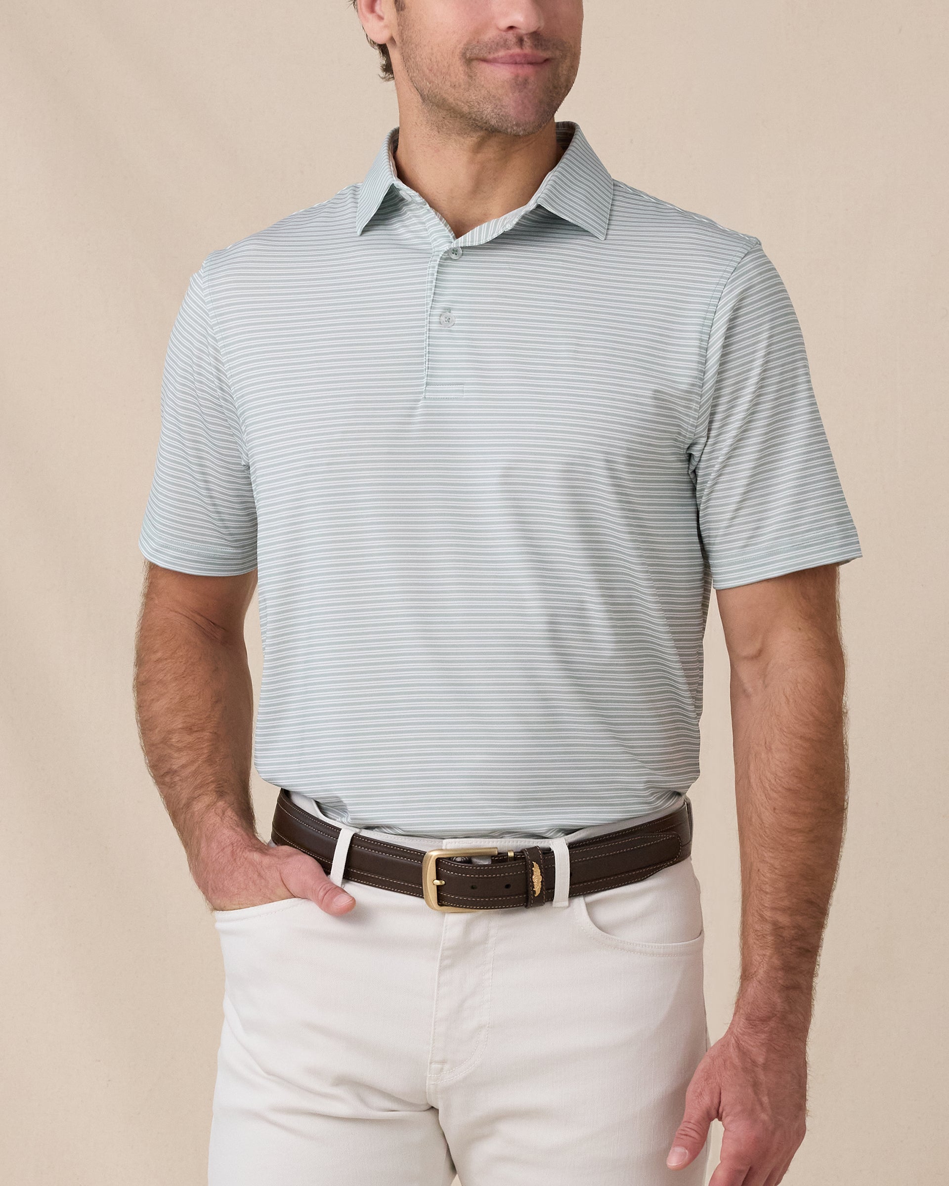 Model wearing the Campus Stripe Polo in Herb with white horizontal stripes, paired with white pants and a brown belt.
