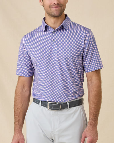 Model wearing the Ironwood Polo in tidal blue with light gray golf bottoms, showcasing the all-over geometric print