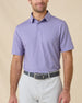 Model wearing the Ironwood Polo in tidal blue with light gray golf bottoms, showcasing the all-over geometric print