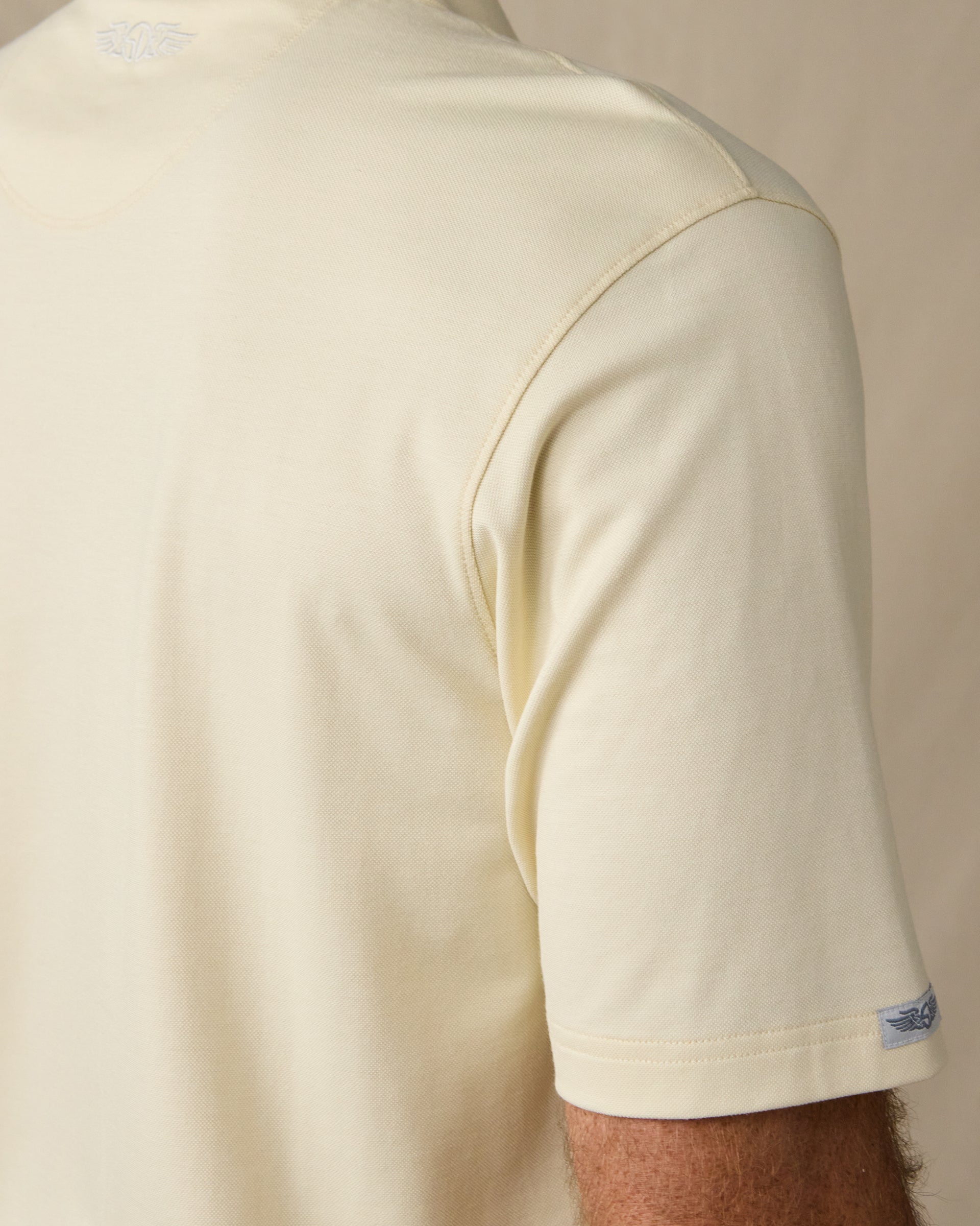 Close-up of the Oxford Polo in Summer Sand, highlighting the shoulder stitching, textured fabric, and Straight Down logo tab on the sleeve.