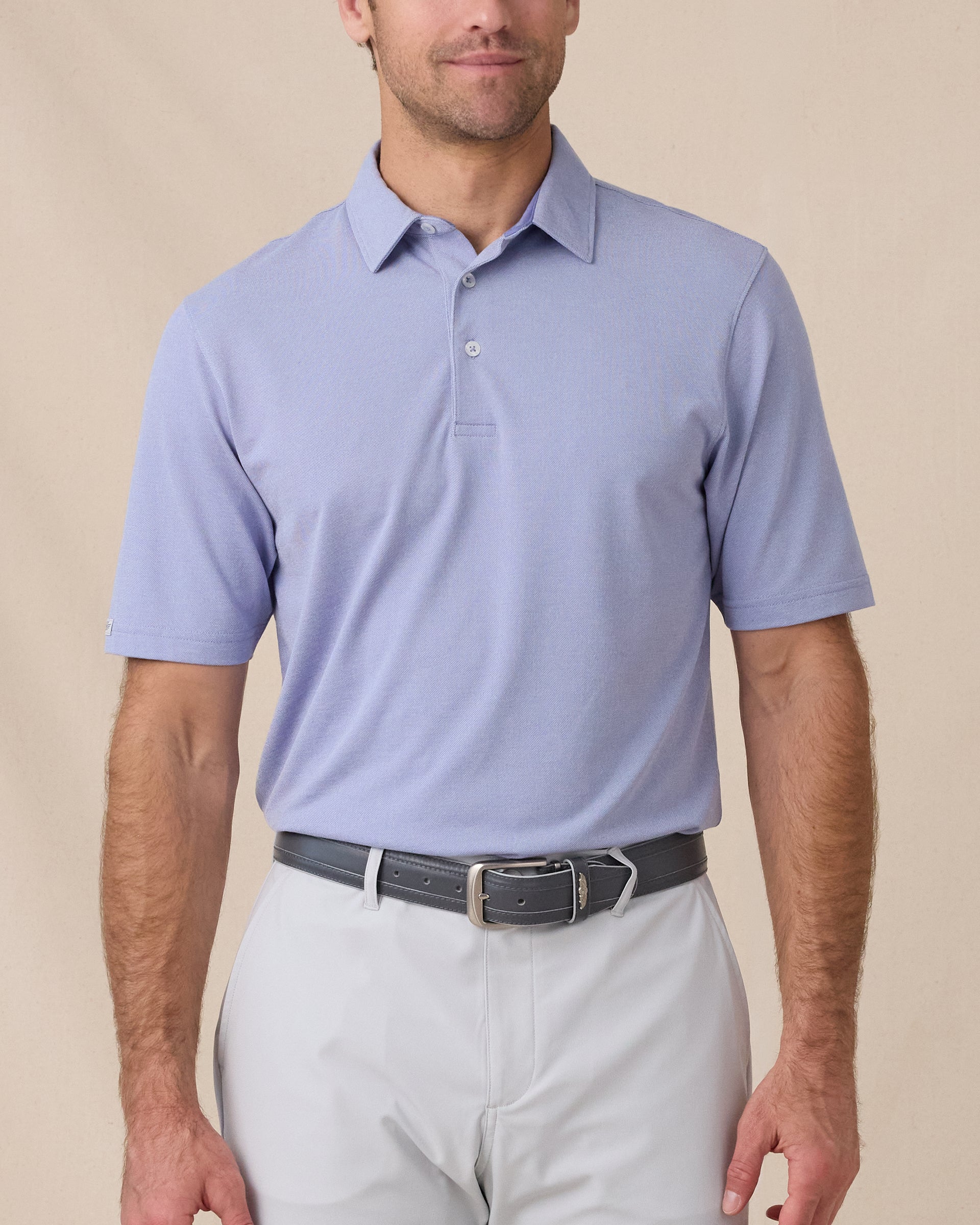 Model wearing the Oxford Polo in chambray blue paired with light gray golf bottoms
