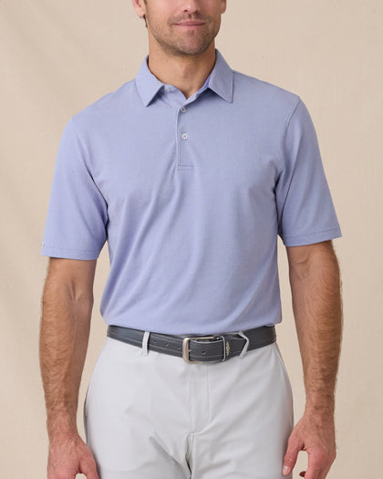 Model wearing the Oxford Polo in chambray blue paired with light gray golf bottoms