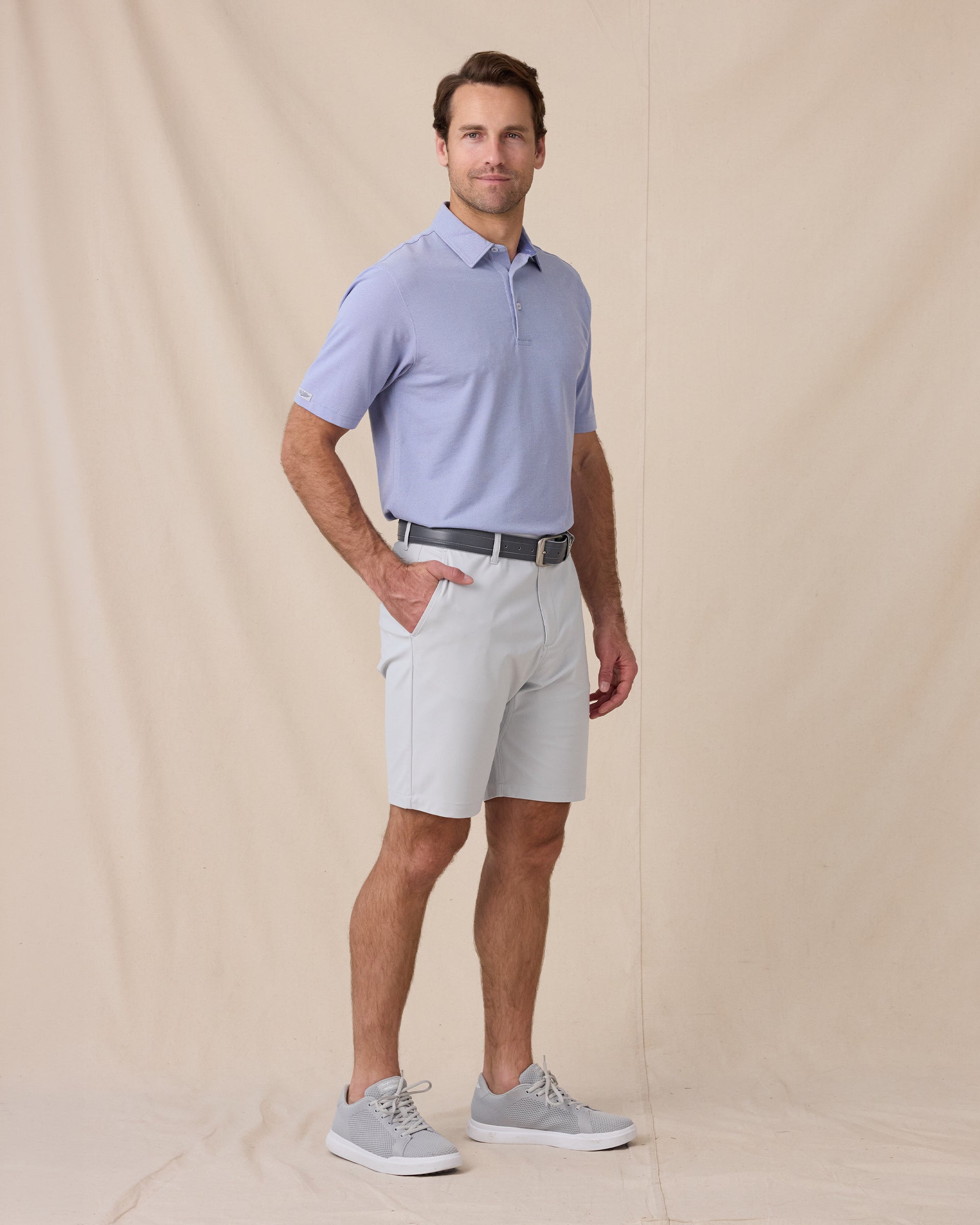 Model wearing the Oxford Polo in chambray blue styled with light gray shorts and golf shoes