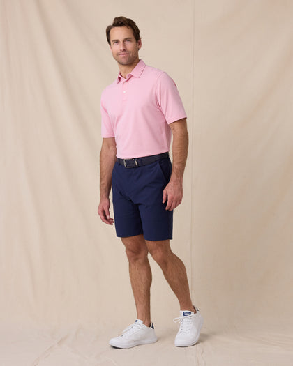 Model wearing the Oxford Polo in punch pink paired with navy golf shorts
